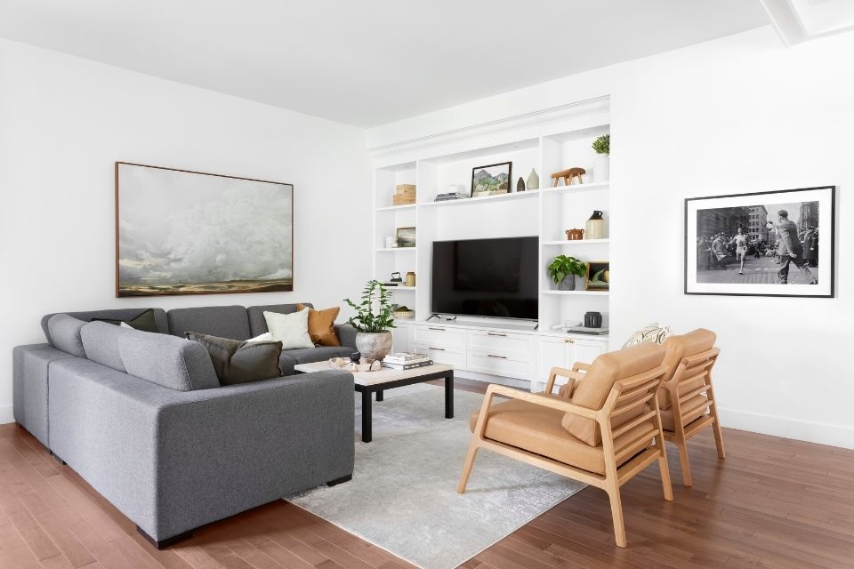Living room with gray sectional, artwork, and leather chairs by Hibou Design + Co.