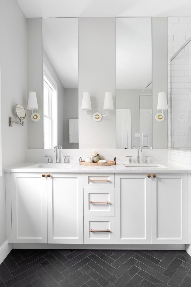 Black herringbone tile pattern and white bathroom cabinets with sconces and mirrors